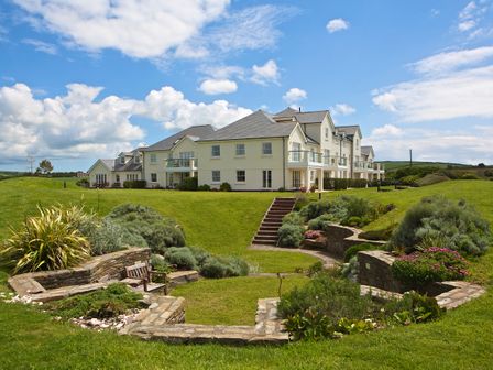 A large white building with multiple windows and balconies surrounded by green lawn and stone garden walls at Ocean View Apartment in Thurlestone