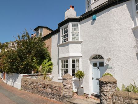 The exterior of a white house with bay windows a light blue door stone fence and plants at The Old Wash House in Dartmouth