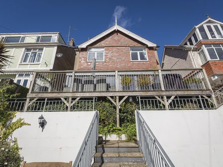 A staircase leading to a wooden balcony with outdoor furniture and plants on a house with brick siding at Prospects in Salcombe