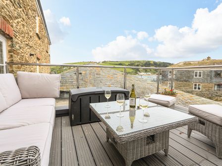 An outdoor seating area with cushioned wicker furniture a glass top table with wine glasses and a bottle on a balcony at Seagulls in Salcombe