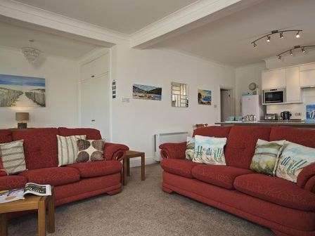 A living room with two red sofas and cushions with a kitchen area in the background at Cove View in Hope Cove