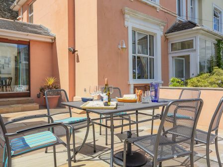An outdoor patio area with a metal table and chairs with cushions a bottle of wine glasses and snacks on the table at Westland in Salcombe