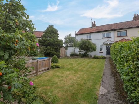 A garden with a lawn a pathway bushes and a white house with a black door at 7 Dale End in Danby near Castleton