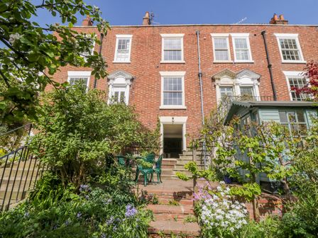 A brick townhouse with white windows a garden shed steps and a patio with garden furniture at Calliope House in Whitby