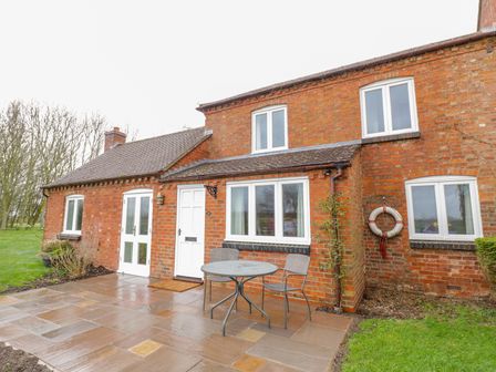 An exterior view of a brick house with a white door and windows a round table with two chairs on the patio at Wigrams Canalside Cottage in Napton-on-the-Hill