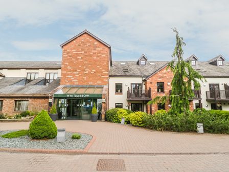 The entrance to a brick and stone building with a green sign reading Whitbarrow and landscaped greenery in front at Ullswater 29 in Penrith