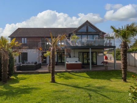 A modern two-story house with a balcony and patio surrounded by palm trees and a lawn at Longmynd in Gloucester