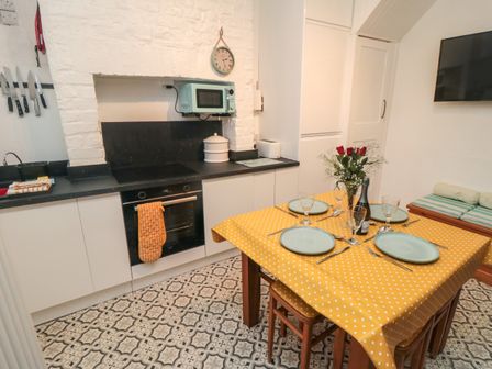A kitchen with a dining table set with plates glasses and cutlery and four chairs with a yellow polka dot tablecloth at Saints Cottage in Scarborough
