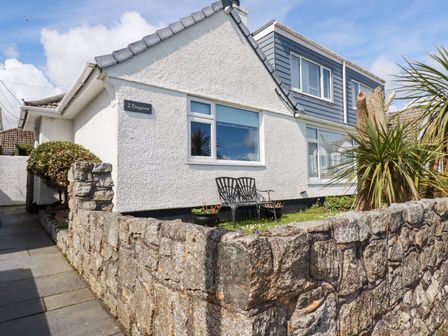 A white house with a stone wall a bench and plants at Bayview Mevagissey
