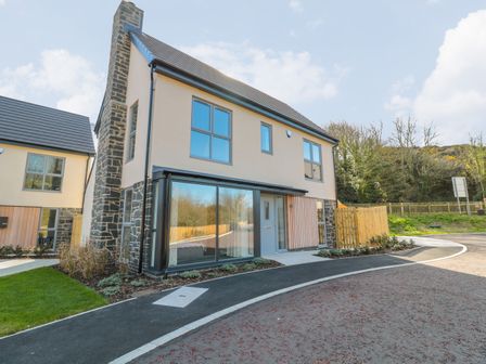 A modern two-story house with large windows and stone chimney near a curved driveway at High Tide House in Craster