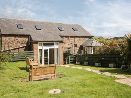 An outdoor garden area with wooden benches stone pathway and a brick building with skylights at Swallows Nest in Armathwaite Cumbria