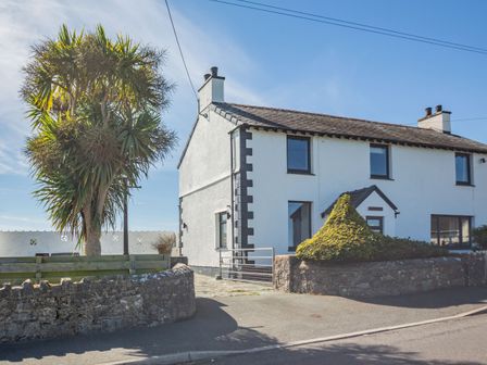 A white semi detached house with a tiled roof a small porch and stone wall along the road at Tyn Y Berth in Benllech
