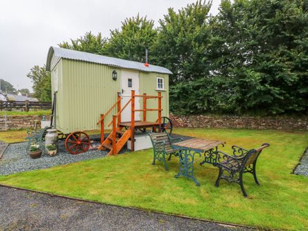 A small green shepherds hut with wooden steps and outdoor seating on grass at Shepherds Hut - The Hurdle in Rosemarket