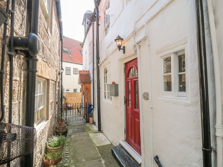 A narrow alley with a red door and potted plants along stone and white walls at Tyreman's Return in Whitby