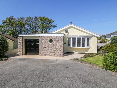 A detached bungalow with a stone garage and driveway with grass and shrubs in front at Croeso in Cemaes Bay