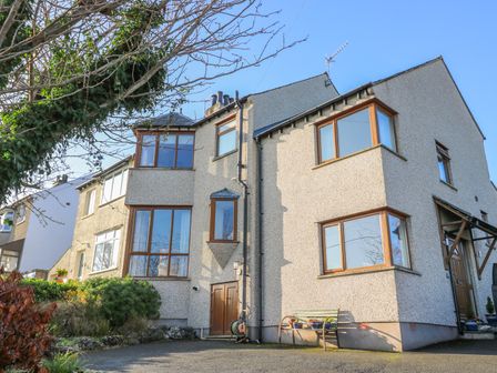 An exterior view of a two story house with pebble dash walls and multiple bay windows with wooden frames at Langtree in Arnside