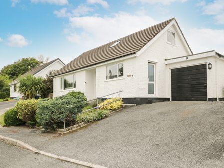 A white house with a driveway garage and shrubs in front at Ty Gilbert in Benllech