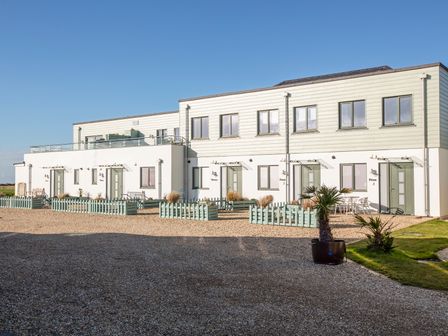 A row of white modern townhouses with green doors and small fenced gardens in front at 4 Ocean Reach in Bolberry