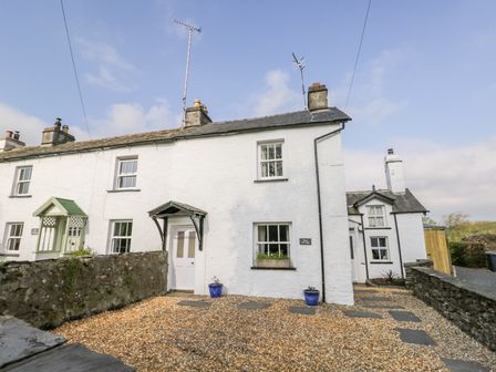 An exterior view of a white terraced cottage with a gravel front yard and stone walls at Rose Cottage in Lowick Bridge