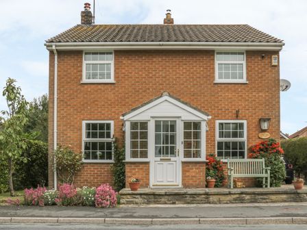 A brick house with a tiled roof a white front porch and door with flower pots and a wooden bench at Humble Bee Cottage in Wold Newton near Hunmanby