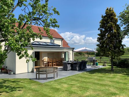 An outdoor patio area with dining tables chairs umbrella barbecue and grassy lawn at The Retreat in Lympsham