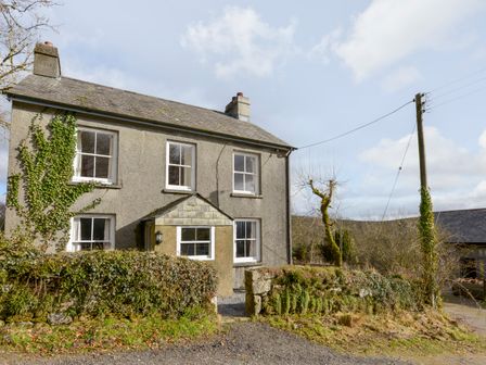 A two-story house with ivy on the wall and a stone fence in front at Brimpts Cottage in Dartmeet