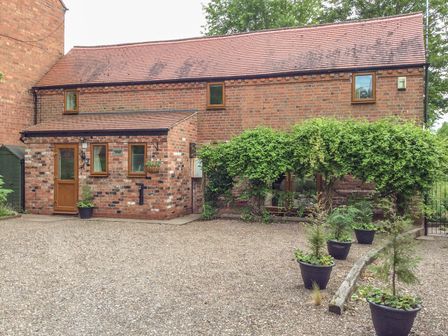 A brick cottage with a tiled roof a door and windows surrounded by potted plants and greenery at Cream Door Cottage in Kidderminster