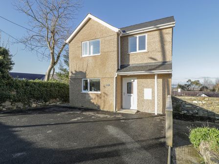 A two-story house with pebble-dash exterior walls white windows and door a paved driveway and a stone wall at Isallt in Rhostryfan near Bontnewydd Gwynedd