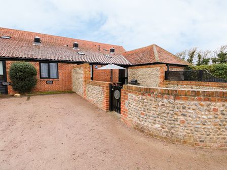 A brick and flint cottage with a tiled roof and an enclosed patio with a gate at Hitchens Cottage in Happisburgh