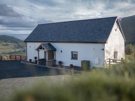 A white barn with a slate roof and small porch surrounded by a wooden fence at Tyn Llwyn Barn in Glyndyfrdwy near Llangollen