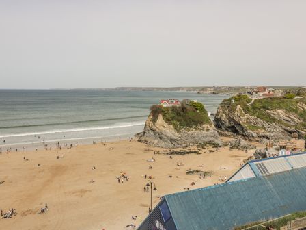 A beach with people, two rocky cliffs with houses on top, and the ocean in the background at Onshore 7 in Newquay