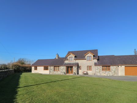 A large house with stone and stucco walls a slate roof and a grass lawn at Afon Rhos Bach in Llanrug