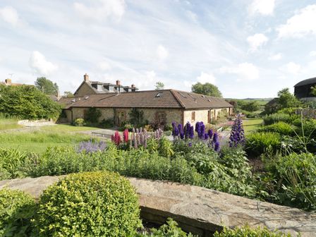 A garden with flowering plants and shrubs in front of a stone building with a tiled roof at Middle Farm Annex in Long Bredy