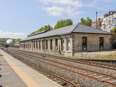 A train station platform beside multiple railway tracks and a long stone building with windows at Repton @ Engine Shed in Whitby