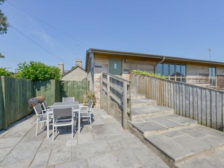 An outdoor patio with a table and six chairs next to a green fence and a wooden building with steps and a ramp at Walnut Cottage in Teigngrace near Newton Abbot