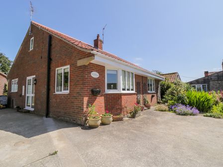 A brick house with a tiled roof and multiple windows surrounded by potted plants and flowers at Runswick in Pickering