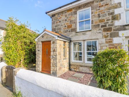 Stone exterior of a house with a wooden door and white framed windows at Miner's Rest in Troon near Camborne