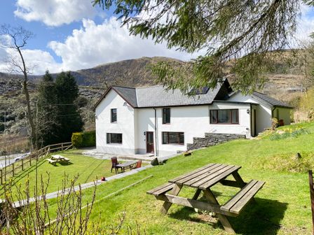 A house with white walls and dark roof surrounded by grass and picnic tables at Stiniog Lodge in Blaenau Ffestiniog