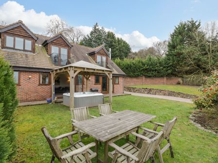 A backyard with wooden table and chairs a hot tub under a wooden gazebo and a brick house at Shatterford Lakes in Shatterford