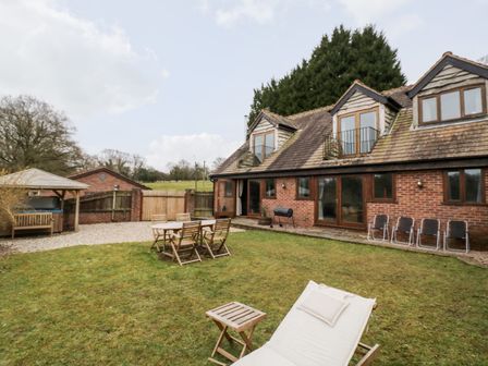 An outdoor garden area with wooden table and chairs lawn chairs and a brick house with three dormer windows at Meadowfall at Shatterford Lakes in Shatterford