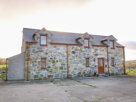 A stone house with a slate roof and wooden window frames surrounding a concrete driveway at Stabl in Pwllheli
