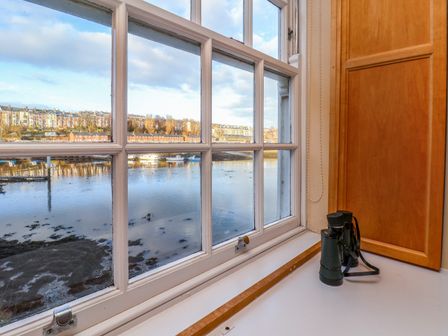 A window with a view of water and buildings outside with binoculars on the windowsill at 5 Old Sail Loft in Whitby