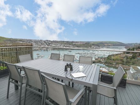 An outdoor dining table with chairs on a balcony overlooking a marina and hills at Moorings in Kingswear Devon