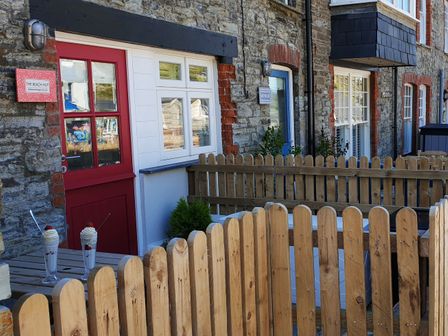 Exterior of cottages with wooden fencing and two milkshakes on a table at Beach Hut in Trebarwith Strand