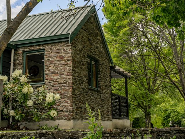A stone cottage with a balcony and flower bushes at Tranquil Tipperary - Arrowtown Holiday Home Arrowtown