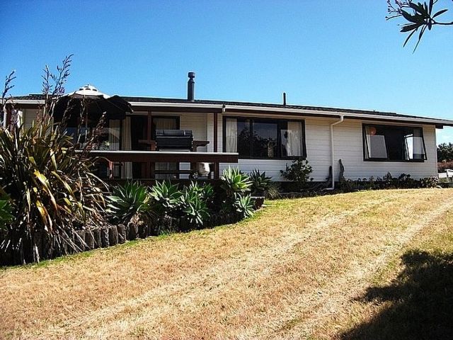 A single-story house with a porch and outdoor furniture surrounded by plants and grass at Relax at Pauanui - Pauanui Holiday Home in Pauanui
