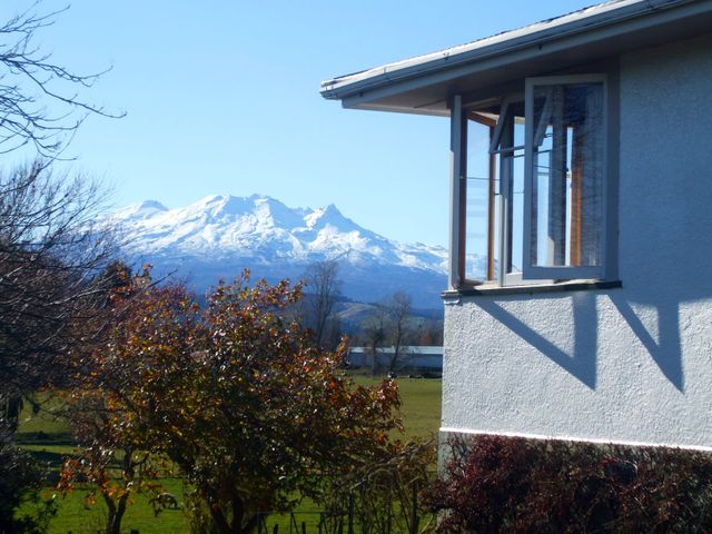 A view of a snow covered mountain with trees and an open window on a white building in the foreground at The Field House - Ohakune Holiday Home in Ohakune