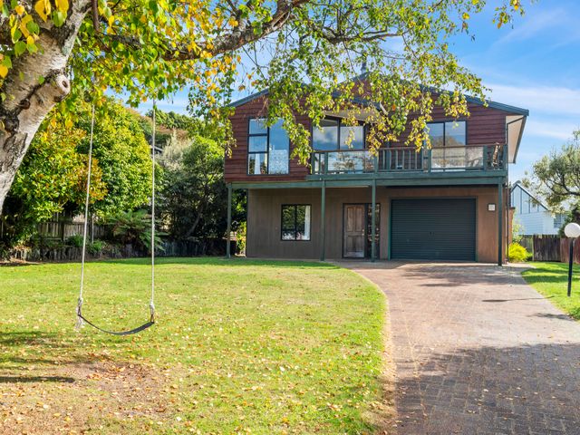 A two-story house with a garage and balcony with a swing hanging from a tree in the front yard at Acacia Views - Acacia Bay Holiday Home in Acacia Bay