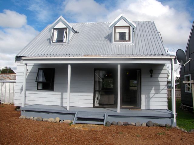 An exterior view of a small house with a metal roof two dormer windows and a front porch with steps at Central Cutie Ohakune