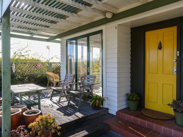 A porch with wooden chairs, table, and potted plants beside a yellow door and glass doors at Jacaranda Lodge - Napier Hill Holiday Home in Bluff Hill